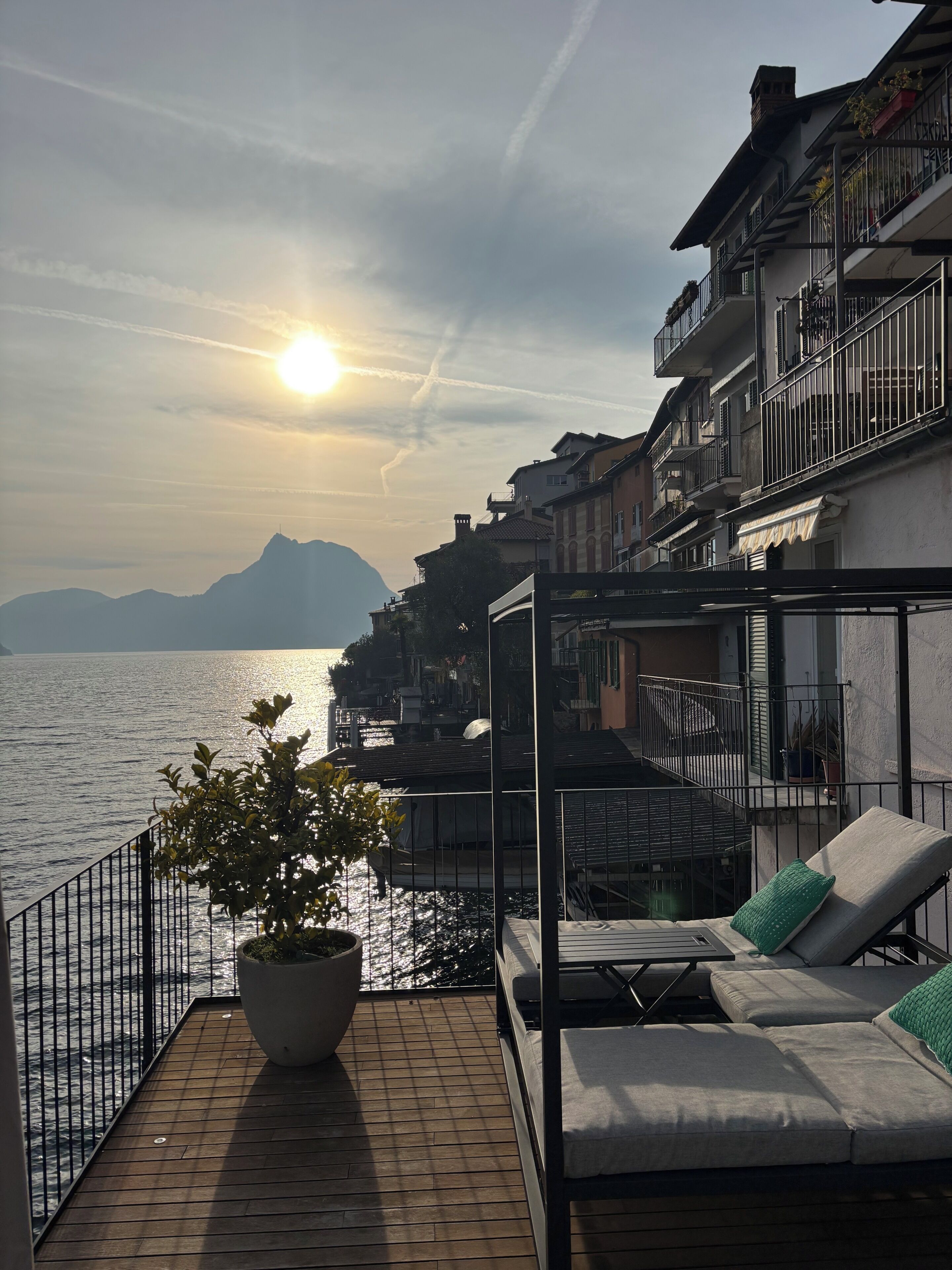Ein Balkon mit Blick auf das Meer und die Berge, ein Blumentopf und eine Sitzecke mit Kissen.