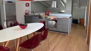 Una cocina moderna con electrodomésticos de acero inoxidable, una lámpara colgante roja y una zona de comedor con sillas rojas.