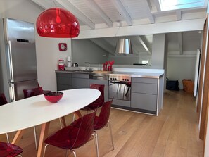 A modern kitchen with stainless steel appliances, a red pendant light, and a dining area with red chairs. - Unique lake house in gorgeous Gandria (Lugano)