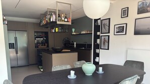 Una cocina moderna con una isla central, electrodomésticos integrados y un comedor con una mesa oscura y sillas grises.