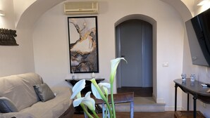 A living room with a sofa, a coffee table with a vase of flowers, a painting on the wall, an air conditioning unit, and a TV on the wall. - IL NIDO DEL DUOMO, cozy apartment in the historic center with a view of the cathedral (Catania)