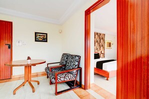 A room with a bed, a chair, a small table, and a door. - Deluxe Collection O Puthali Park (Mysore)