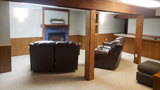 A living room with a fireplace, leather sofas, wooden beams, and a kitchen area. - Basement Rental for EAA. 4.2 miles from EAA. (Oshkosh)
