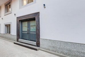 Un bâtiment doté d’une grande porte de couleur sombre, d’une petite fenêtre ornée de barreaux en métal et d’un mur à la texture particulière.