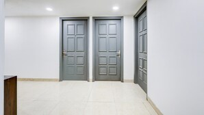 A hallway with two grey doors, white walls, and a tiled floor. - Classic With Balconyshalimar Bagh (New Delhi)