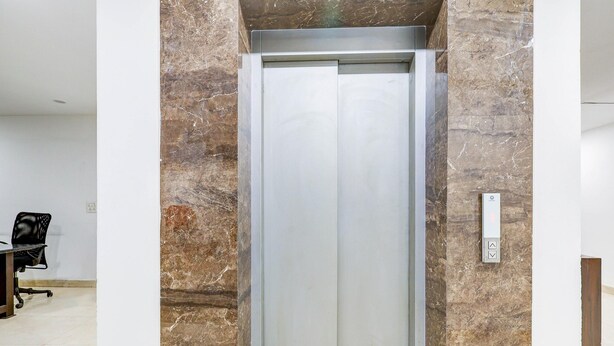 An elevator in a modern interior with marble walls and a plain office chair. - Classic With Balconyshalimar Bagh (New Delhi)