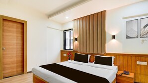 A hotel room with a large bed, wooden headboard, bedside tables, and a window with blinds. - Super Townhouse Formerly Silver Crest (Pune)