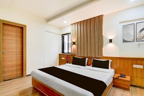 A hotel room with a large bed, wooden headboard, bedside tables, and a window with blinds. - Super Townhouse Formerly Silver Crest (Pune)