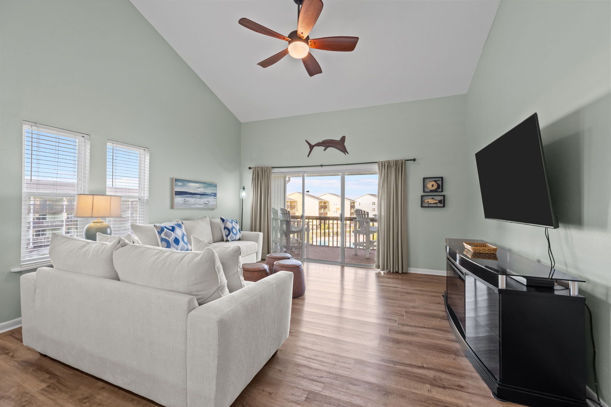 A living room with a ceiling fan, a sofa, a TV, and a balcony with a view.