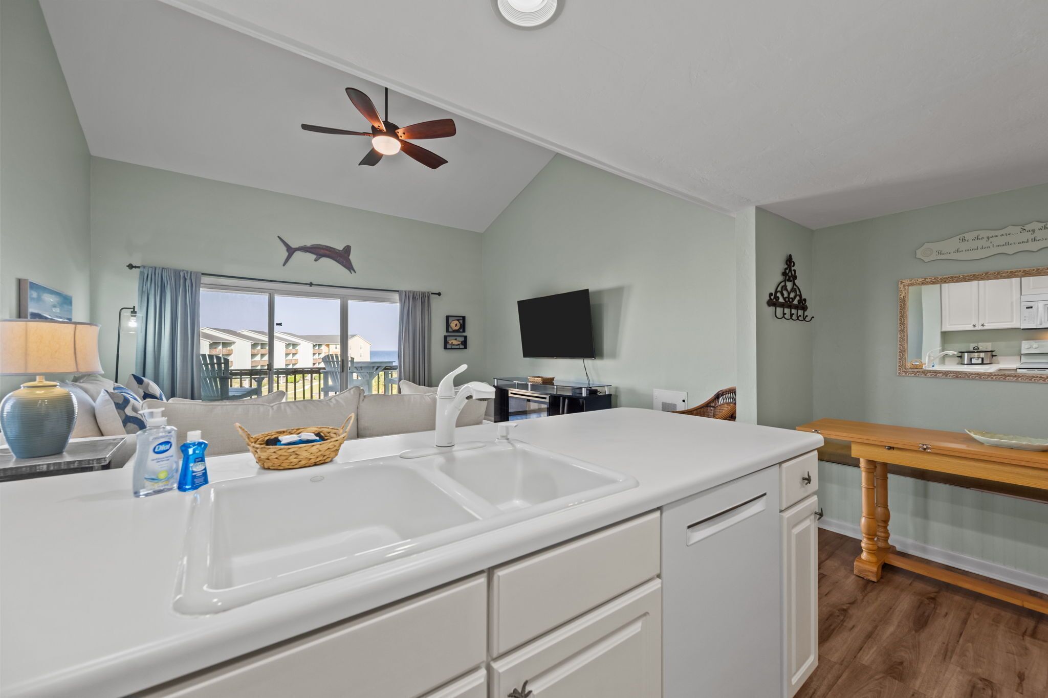 A modern kitchen with a white countertop, a ceiling fan, a large window with curtains, and a view of the outside.