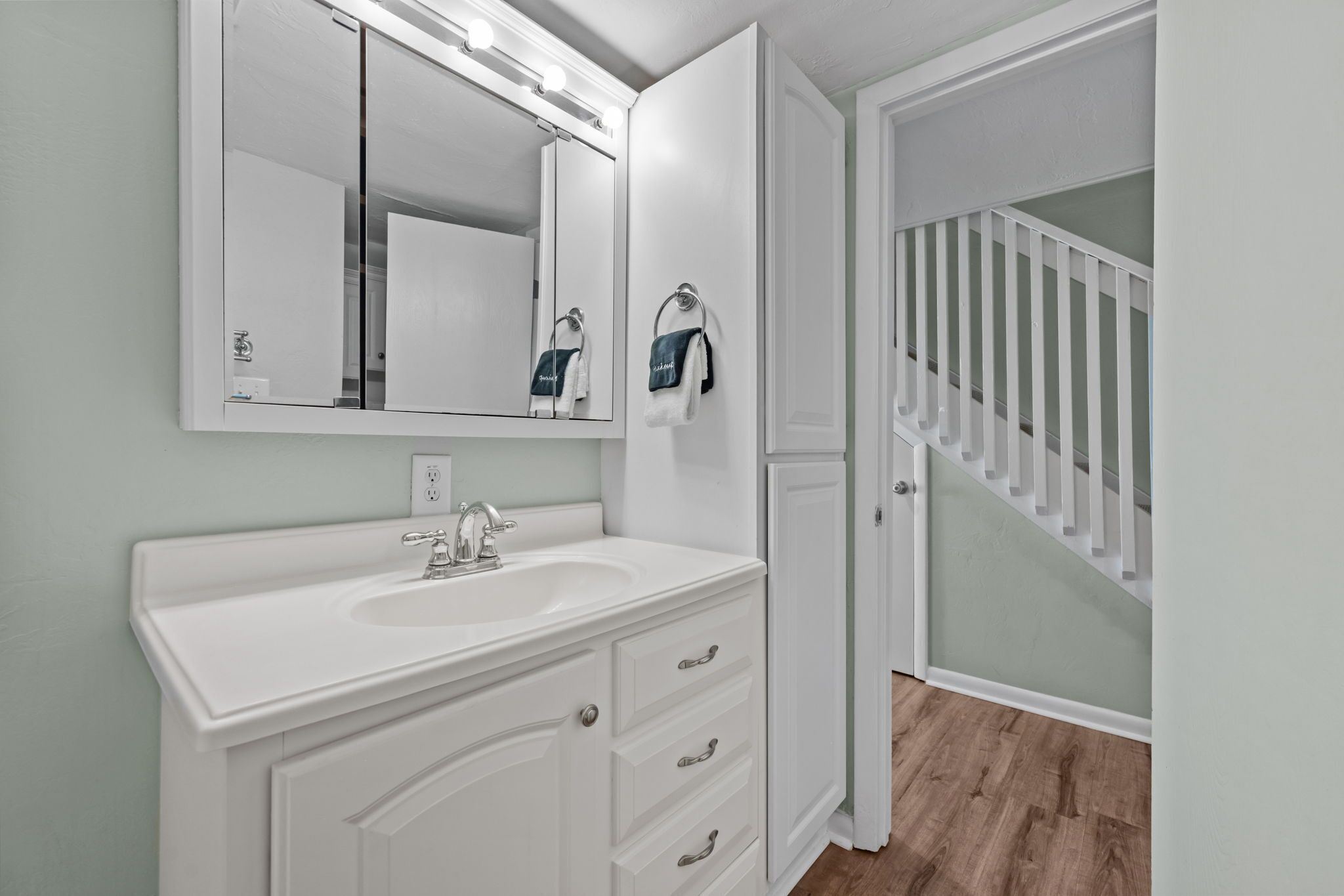 A bathroom with a white vanity, a large mirror, and a staircase leading to another room.