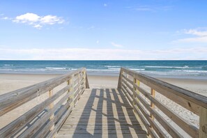 A wooden boardwalk leading to a beach with the ocean in the background.
