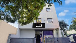 A modern hotel entrance with a sign reading 'HOTELO Company-Serviced,' a gated driveway, and a tree in the foreground. - Saver Double White Solitaire (Ludhiana)