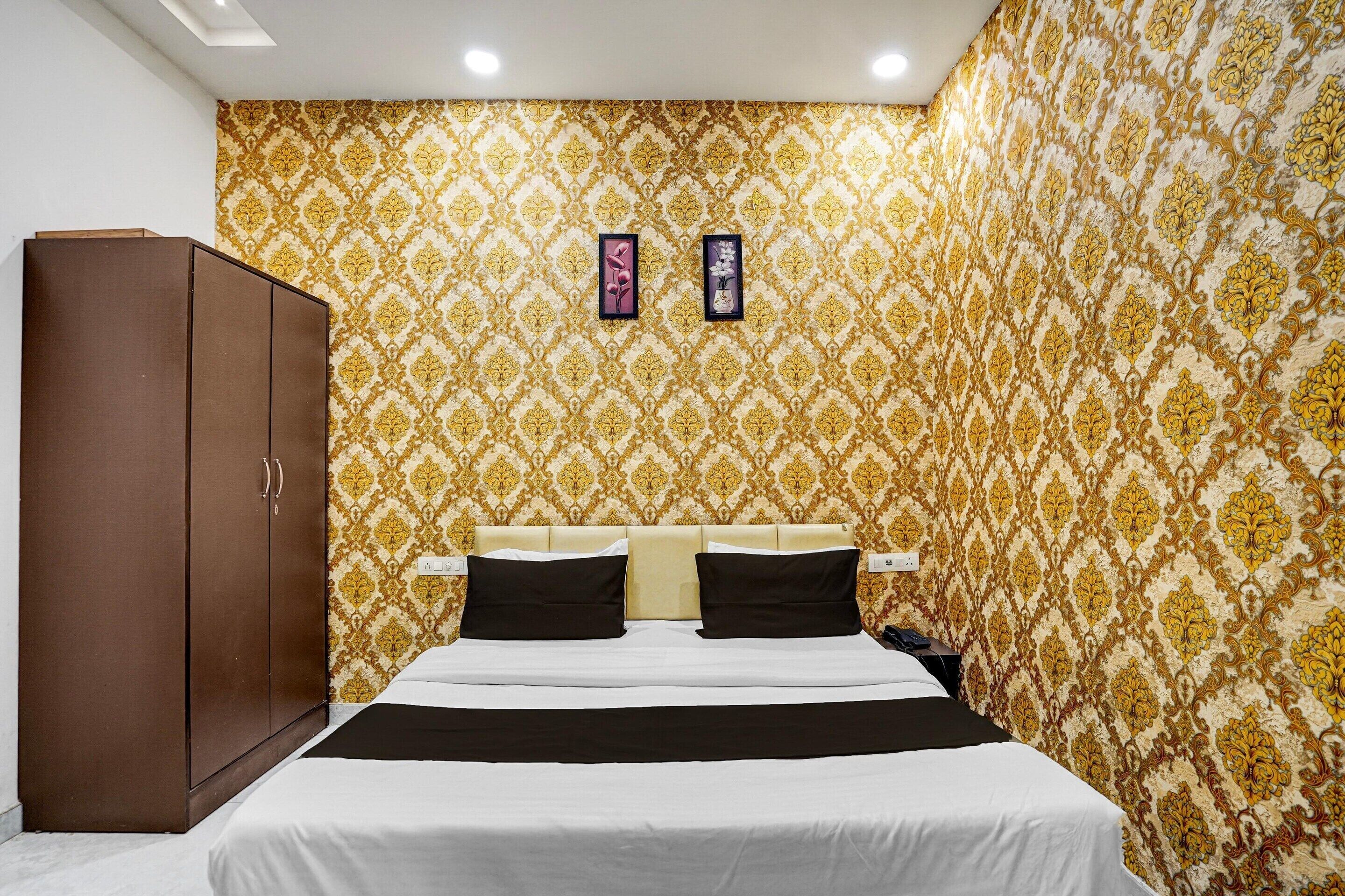 A bedroom with a patterned wallpaper, a bed with white and black bedding, a brown wardrobe, and two framed pictures on the wall.