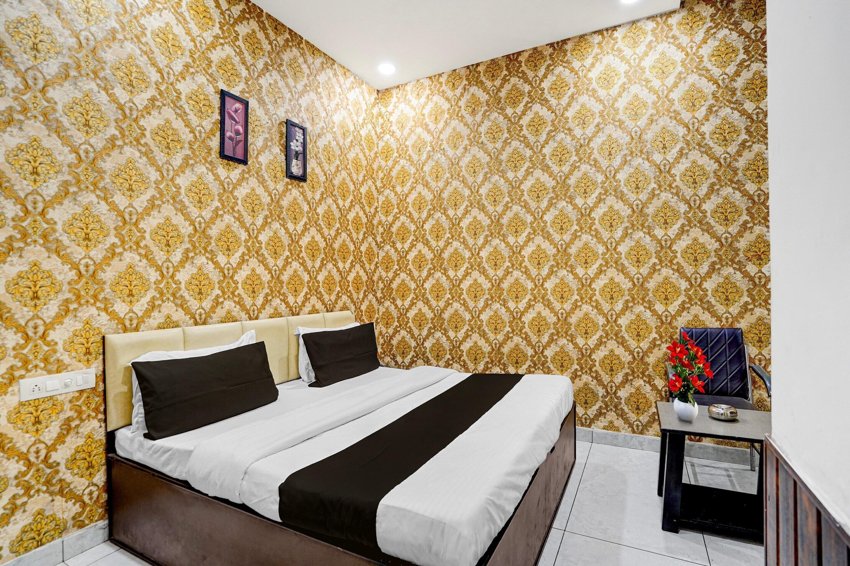 A bedroom with a bed, a bedside table with a vase, and patterned wallpaper.