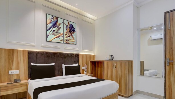 Een moderne hotelkamer met een groot bed, een houten hoofdbord, een nachtkastje, een houten garderobe, een spiegel en twee wanddecoraties.