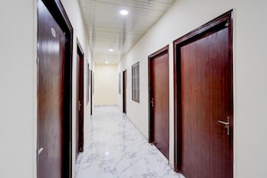 Un pasillo con puertas de madera, paredes blancas y suelo de mármol.