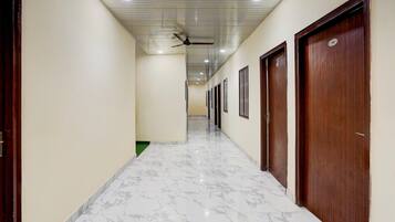 A corridor with a ceiling fan, wooden doors, and a marble floor.