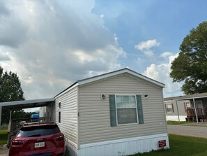 A single-story mobile home with a pitched roof, a window with shutters, and a visible garage door.