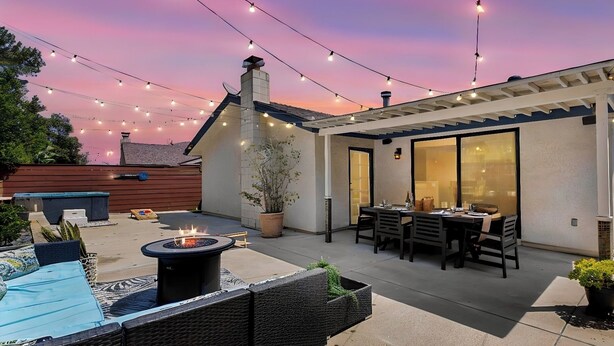 Eine Terrasse mit Gartenmöbeln, einem Feuerkorb und Lichterketten vor einem Sonnenuntergangshimmel.