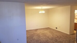 A room with beige carpet, white walls, a chandelier, and a door leading to another room. - Spacious 3BR | Perfect for July Visitors (Newark)