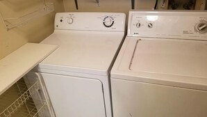 Two white front-loading washers in a laundry room with a metal shelf and a metal rack. - Spacious 3BR | Perfect for July Visitors (Newark)