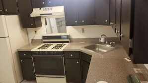 A compact kitchen with a stove, oven, sink, and dark cabinets. - Spacious 3BR | Perfect for July Visitors (Newark)