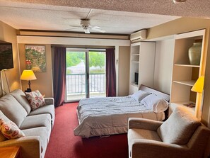 Ein Hotelzimmer mit einem Bett, zwei Sesseln, einem Sofa, einem Fernseher, einem Deckenventilator und einem Balkon mit Blick.