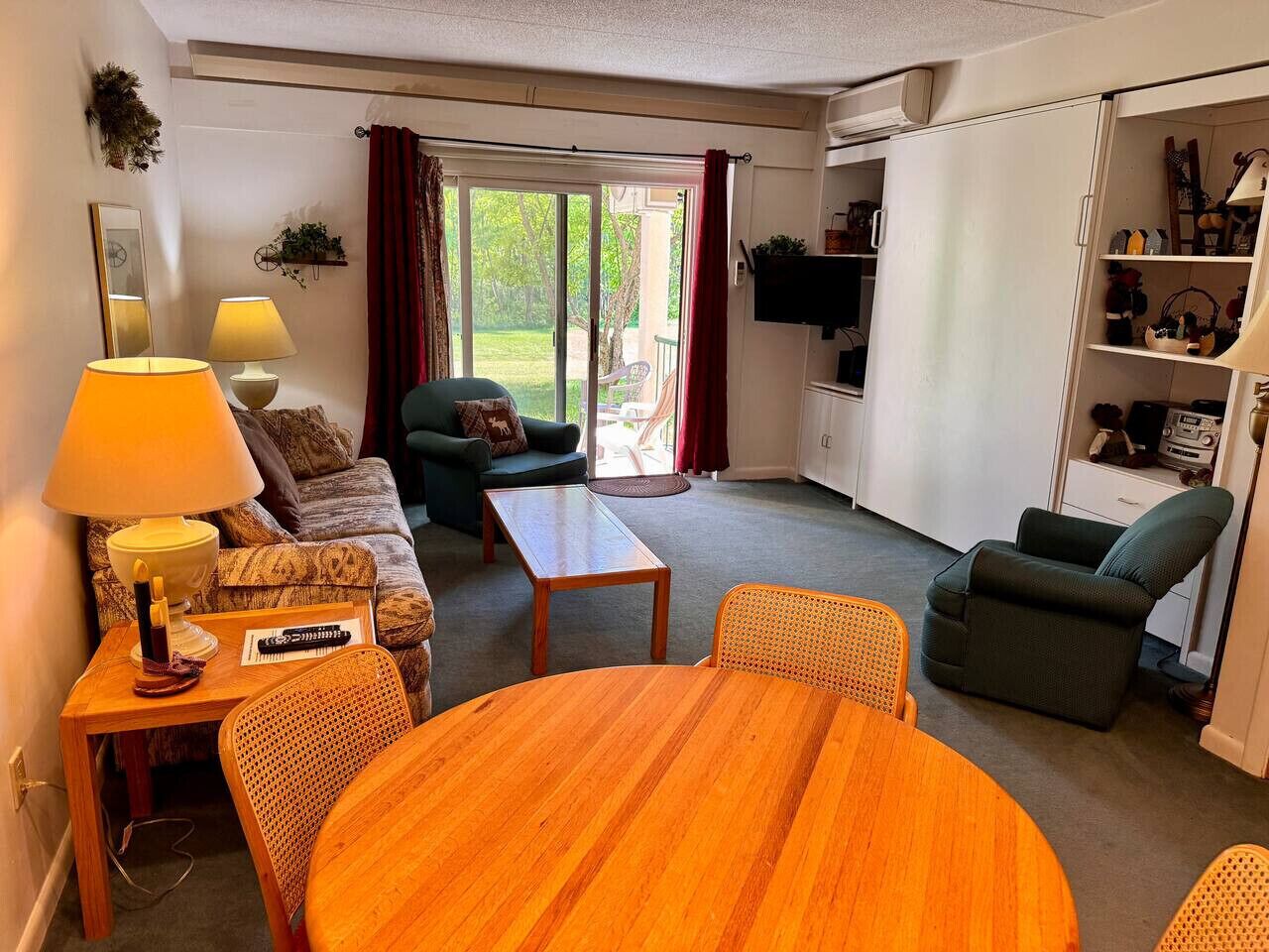 A living room with a sofa, a dining table, a chair, a lamp, and a television.