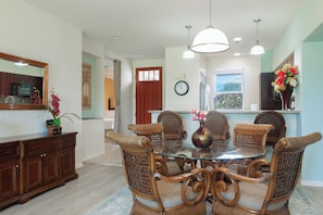 A dining area with a glass table surrounded by wicker chairs, a wooden cabinet, and a vase with flowers. -  Beautiful condo walking distance to the beach, shops and restaurants (Waikoloa Village)