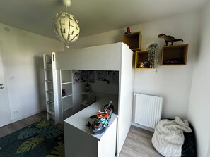 Ett rum med en våningssäng, ett skrivbord med en modell av ett skepp, hyllor med leksaker och ett element.