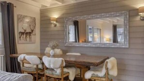 Un comedor con una mesa y sillas de madera, un espejo grande y apliques de pared.