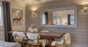 A dining area with a wooden table and chairs, a large mirror, and wall-mounted sconces. - Charming apartment in the heart of Megève with terrace and mountain view (Combloux)