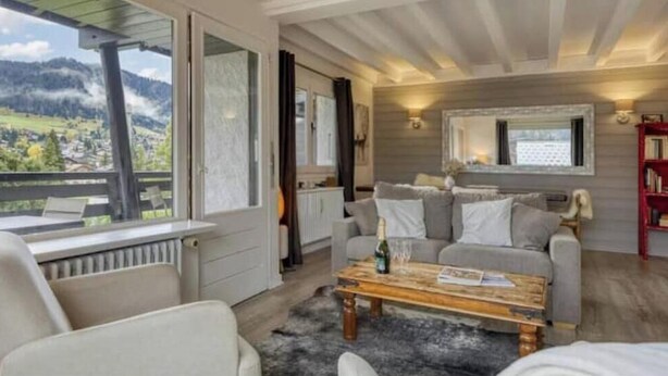 Una sala de estar acogedora con un sofá, una mesa de centro y vistas a un paisaje montañoso a través de grandes ventanales.