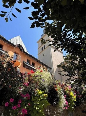 A building with a bell tower, surrounded by lush greenery and flowering plants. - Charming apartment in the heart of Megève with terrace and mountain view (Combloux)