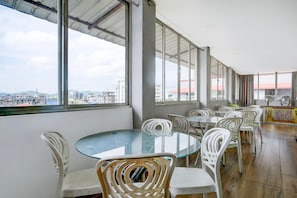 A spacious balcony with a glass table and white chairs, overlooking a cityscape. - Classic With Balcony Beltola Tiniali Pratishtha (Guwahati)