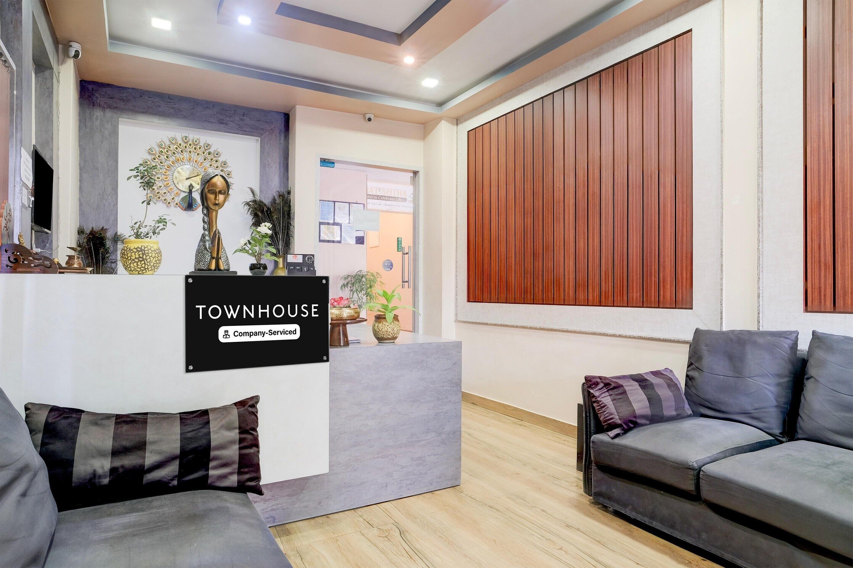 A reception area with a sign reading 'TOWNHOUSE Company-Serviced,' a reception desk, a peacock wall decoration, and a wooden panel wall.