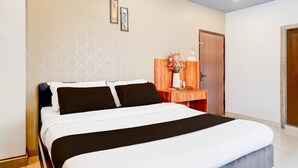 A hotel room with a large bed, a wooden desk, a mirror, and a door. - Classic With Balcony Beltola Tiniali Pratishtha (Guwahati)