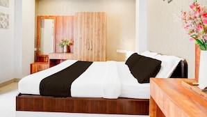A hotel room with a bed, a wooden nightstand, a mirror, a vase with flowers, and a wall with a textured pattern. - Classic With Balcony Beltola Tiniali Pratishtha (Guwahati)