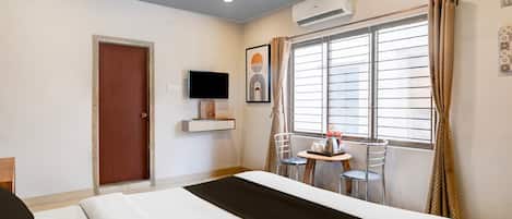 A hotel room with a bed, a TV, a window with curtains, and a small table with a chair.