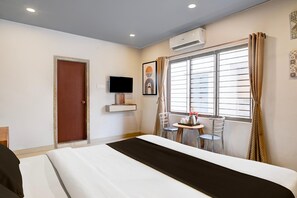A hotel room with a bed, a TV, a window with curtains, and a small table with a chair. - Classic With Balcony Beltola Tiniali Pratishtha (Guwahati)