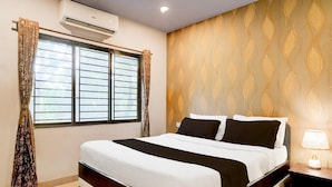 A hotel room with a bed, curtains, an air conditioner, a patterned wall, and a nightstand with a lamp. - Classic With Balcony Beltola Tiniali Pratishtha (Guwahati)