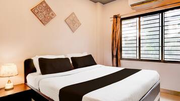 Una habitación de hotel con cama, mesita de noche, lámpara y ventana con cortinas.