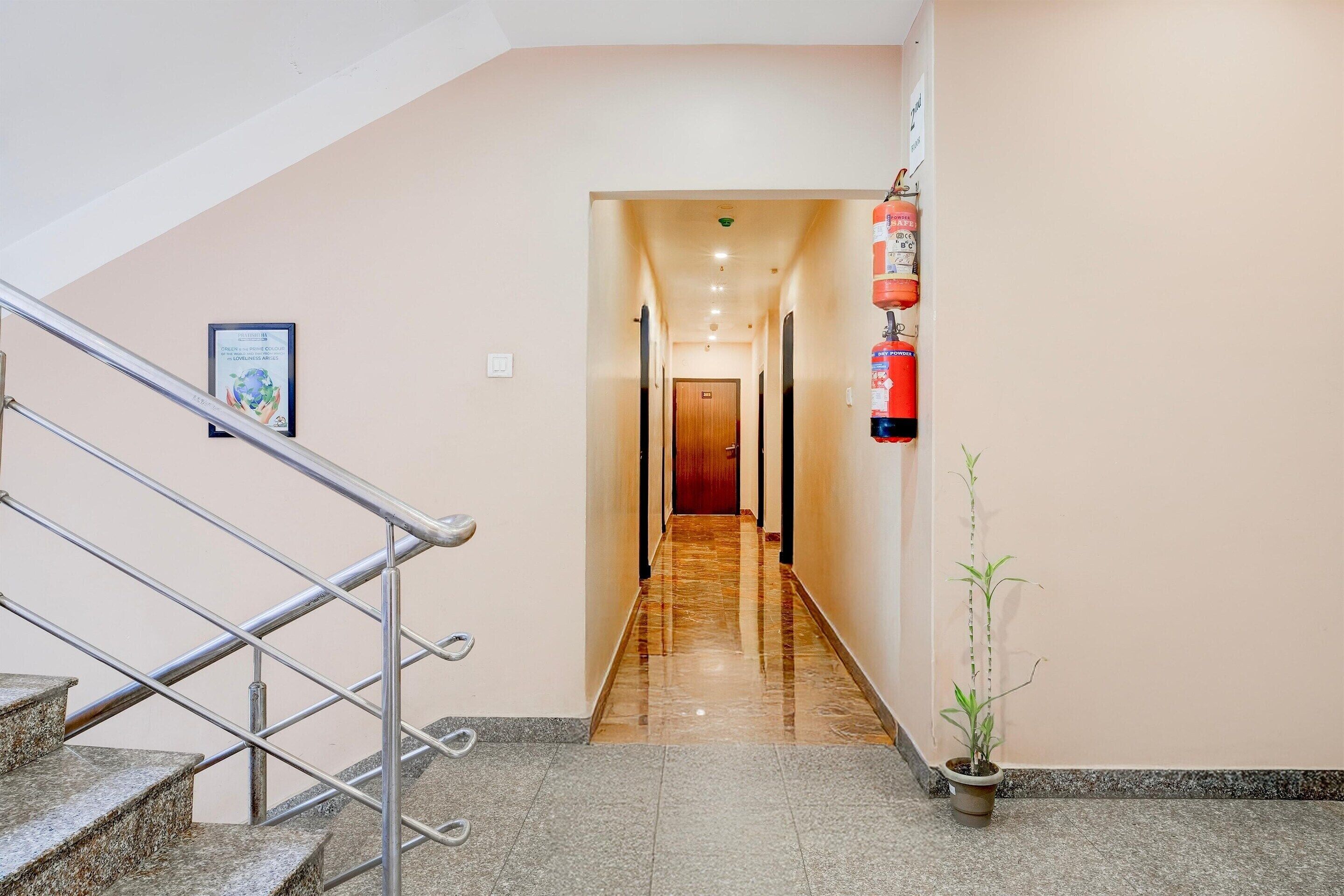 Un pasillo de hotel con una escalera a la izquierda, un extintor a la derecha y una puerta al final.