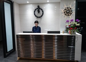 A reception desk with a modern design, a clock on the wall, and a decorative vase with flowers. - Ehouse Hotel Xining Banch (Taipei)