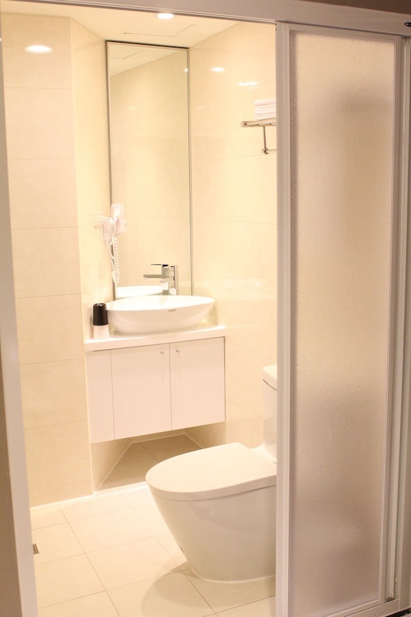 Ein Badezimmer mit weißem Waschbecken, einem Spiegel, einer Toilette und einer Duschkabine.