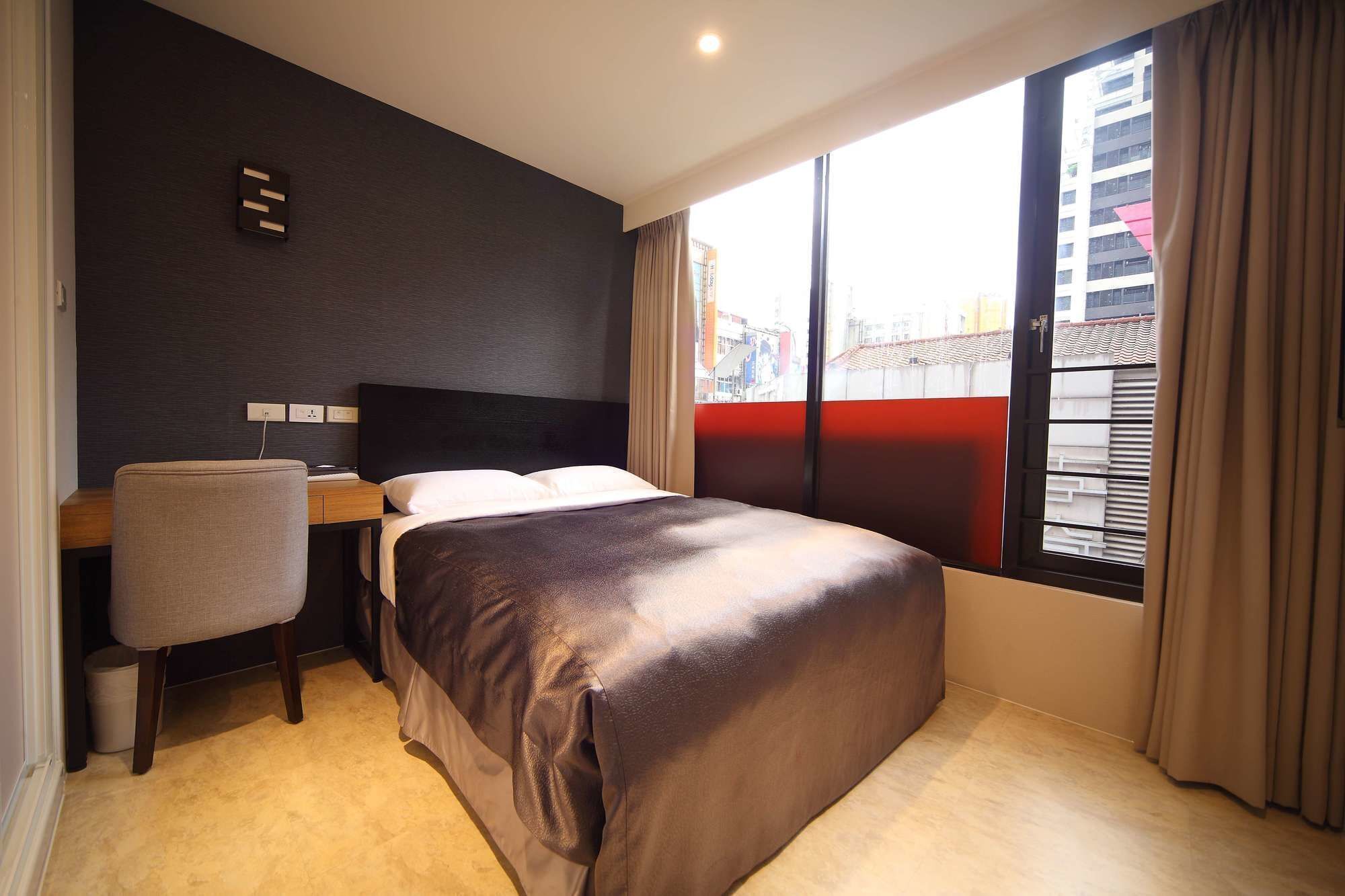 A hotel room with a bed, a desk, a chair, a window with curtains, and a city view.