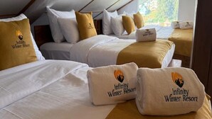 Ein Hotelzimmer mit zwei Betten, jeweils mit weißer Bettwäsche und einem braunen Kopfteil. Auf den Betten liegen Handtücher mit dem Logo des Infinity Winter Resorts.