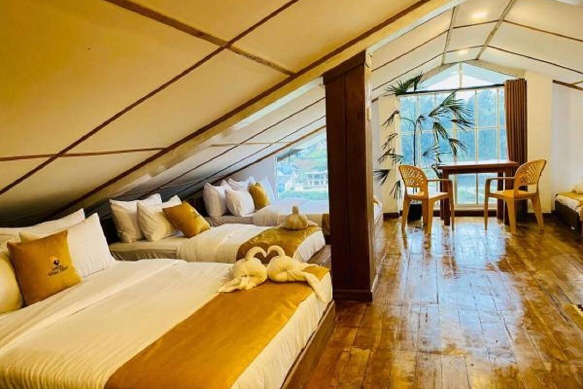 Habitación de hotel con techo inclinado, dos camas con sábanas blancas, suelo de madera, zona de comedor con mesa y sillas, y vista por un ventanal grande.