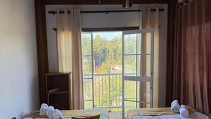 Ein Zimmer mit zwei Betten, einer Holzablage und einem großen Fenster mit Blick auf Bäume.